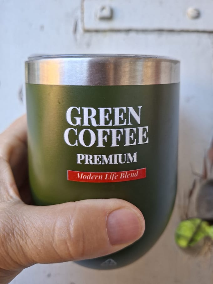 Eine Hand hält einen olivgrünen Green-Coffee-Premium-Becher mit Modern Life Blend